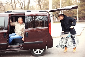 Young man loading wheelchair of handicapped man into Senior Citizen Transportation