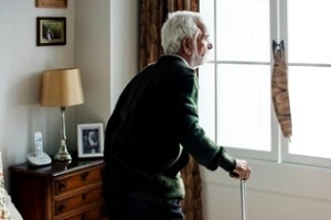 old man standing and looking out of window