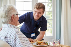 care worker serving dinner to a aging parents at his home