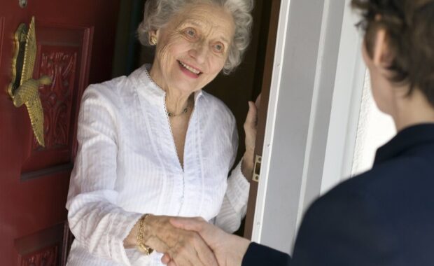 smiling senior woman greeting visitor at the front doo