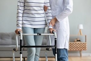 caregiver helping to disabled aged female patient walk with walker physical therapist teach her