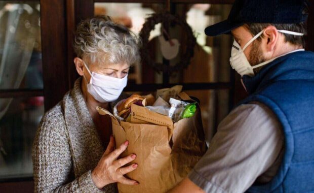 courier delivering shopping to senior woman with face mask