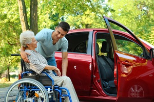 man helping disabled senior woman in wheelchair to get into car outdoors