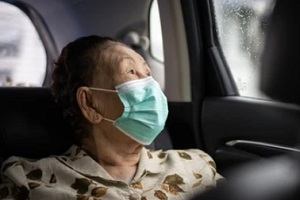 old lady wearing mask in back seat of a car