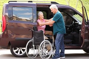 man helping senior woman to get out from van into wheelchair
