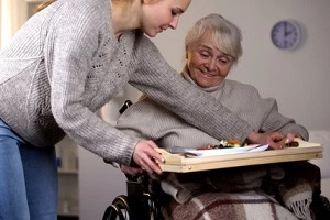 girl helping senior women in wheelchair with dinner