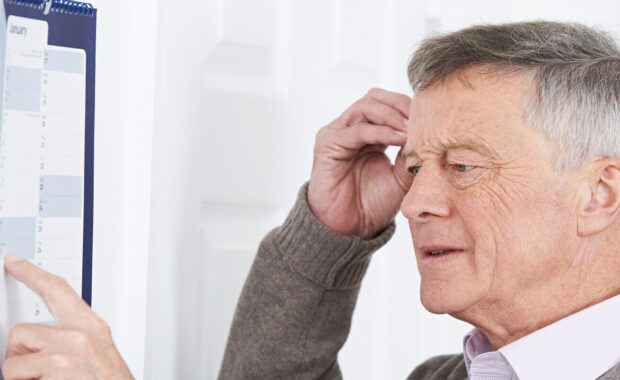 confused senior man with dementia looking at wall calendar