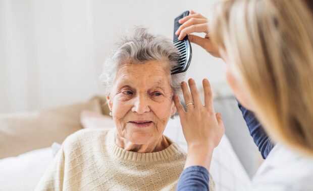 health visitor combing hair of senior woman at home