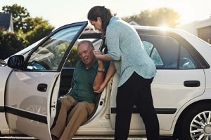 women taking senior man out of the car