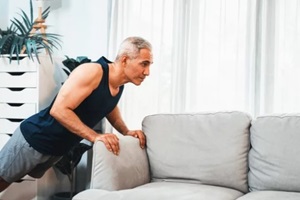 active senior man using furniture for effective targeting muscle with push up at home exercise as concept of healthy fit body lifestyle after retirement