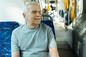 elderly man is using wireless earbuds during ride in public transport