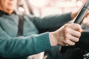 close up of senior man holding hands on steering while and driving his car