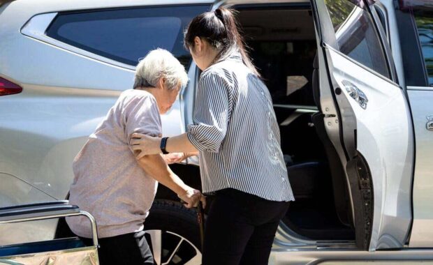 asian female caregiver helping disabled elderly woman in wheelchair to get into the car