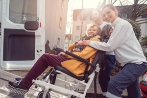 senior woman in wheelchair being picked up by team from transport service