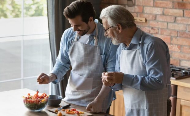 happy elderly Caucasian father and adult son cook tasty dish together in home kitchen