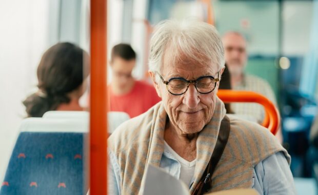 senior man reading book while traveling with bus