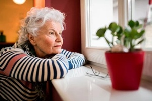 sad alone senior woman looking through window