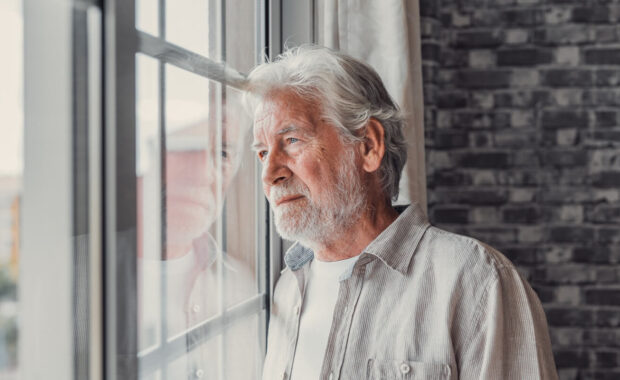 elderly mature senior man in eyeglasses looking in distance out of window