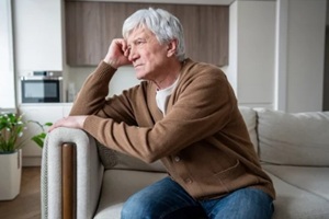 aging senior man sits alone in empty living room staring vacantly, struggling with memory loss