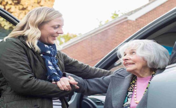 Female Volunteer Driver Helping Senior Woman Coming Out from Car
