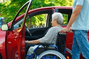 Young Driver Helping Disabled Senior Woman on Wheelchair to Get into senior citizen transportation