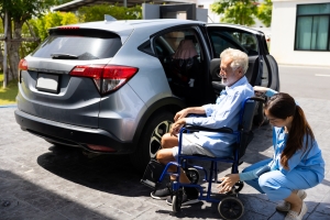 Female Caregiver Helping Disabled Senior Man Get Into Car