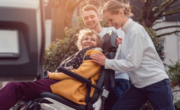 Two Helpers Picking Up Disabled Senior Woman for Transport