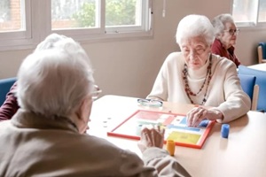 senior woman playing ludo with friends at table in nursing home