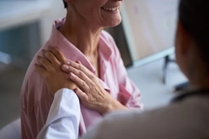 aged Caucasian woman sitting in medical office receiving comforting touch from female doctor
